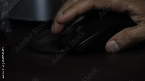 Close up of a hand holding and clicking a black computer mouse in a dark room