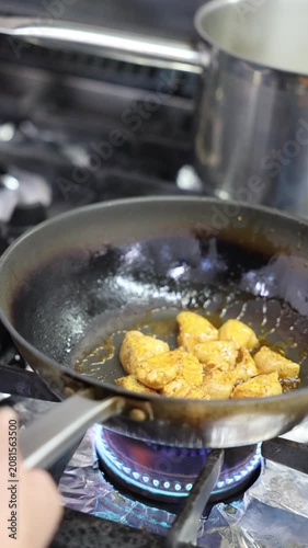 Chicken pieces cooking in a frying pan over a blue gas flame on the stove