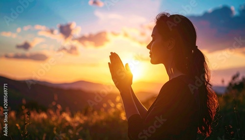 A woman in profile, backlit by a sunset, hands clasped in prayer, with mountain backdrop