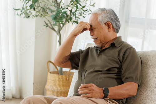 Fotografie Senior Man with Head Pain and Fatigue Sitting Alone at home, elderly health discomfort, headache symptoms, stress, and senior wellness concerns