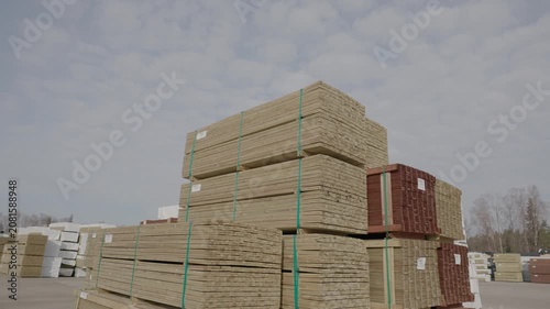 Large stacks of bundled wood planks stored in an open-air lumber yard under a cloudy sky, ready for transport, distribution, or construction use