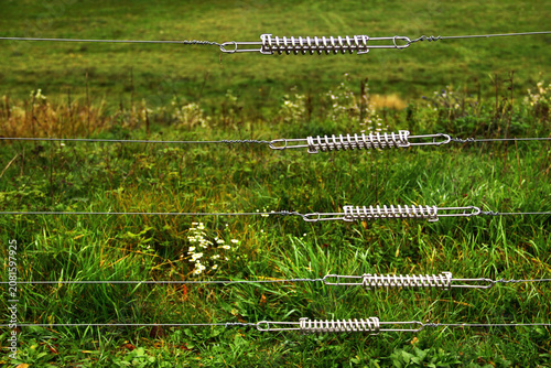 Electric pasture fence with tension springs across green meadow in rural countryside