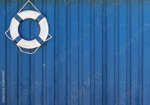 White lifebuoy hanging on blue wooden wall with copy space