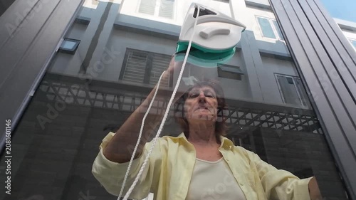 Concentrated woman spends weekend cleaning house with modern magnetic gadget. Female housekeeper works hard, cleaning house windows carefully to achieve spotless glass and perfect domestic order.