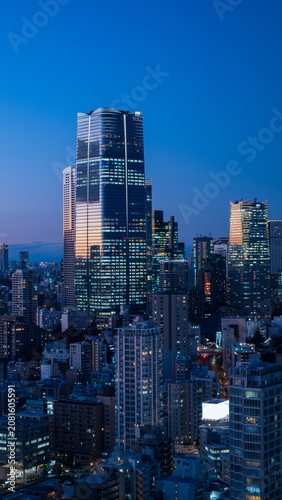 Modern Tokyo cityscape at dusk during the magic hour, featuring the illuminated Azabudai Hills skyscraper and surrounding city lights.