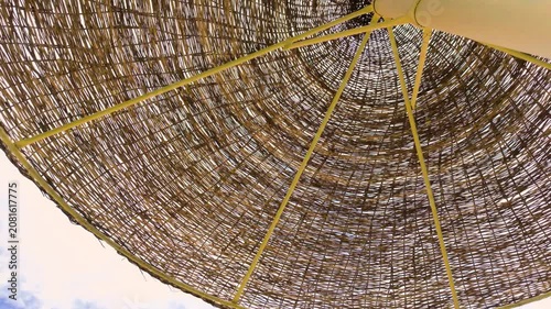 Slow motion footage of abstract close up of a woven straw beach parasol canopy in Sharm El Sheikh Egypt with natural textures and minimal tropical seaside design against a bright sky
