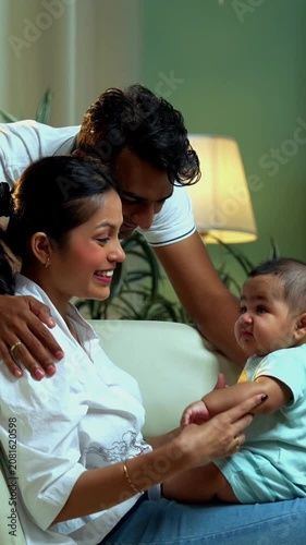 Indian parents catching baby boy while sitting on sofa in modern living room, enjoying fun family bonding, joyful parenthood, love, laughter, care, connection, parenting moments indoors at home