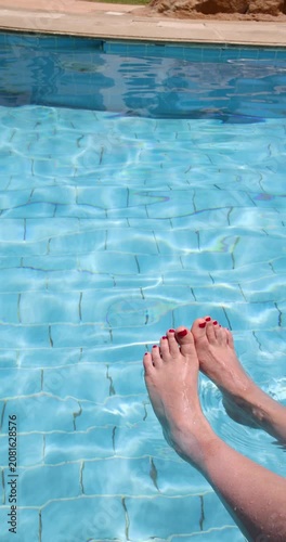 Slow motion portrait footage of a woman with red nail varnish relaxing with feet in clear swimming pool water at a luxury resort in Egypt during summer holiday with shimmering reflections