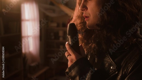 Young man with long curly hair wearing leather jacket singing passionately into microphone. Clip for music industry promos, audio gear ads, or creative lifestyle campaigns