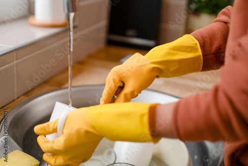 Tableau sur toile Person washes dishes in a kitchen sink while wearing yellow rubber gloves during