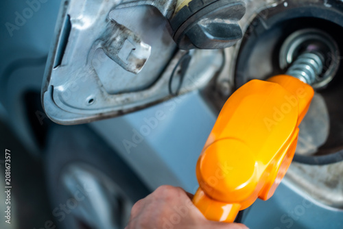 Close up of gas station worker holding gas fuel pump, filling car tank. Automotive refueling, petrol station service, and transportation concept in vibrant outdoor.