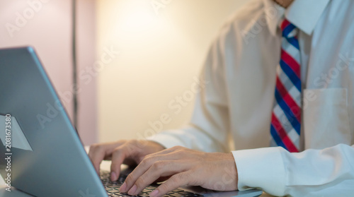 Close up of businessman wearing tie and white shirt working on laptop at table . Typing on keyboard while working from home, remote business and productivity concept.