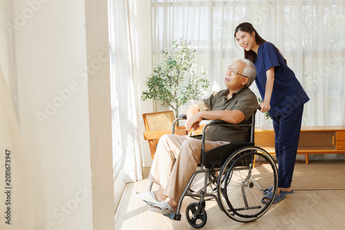 Obraz na plátně Female caregiver assists an elderly man in a wheelchair during a nursing at home visit, home care, senior care, wheelchair assistance, mobility support, and compassionate home healthcare