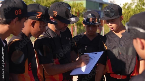 Focused coach drawing a game plan on a clipboard, instructing and mentoring his young team of boys during a sunny day baseball practice