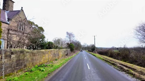 Driving dash cam style footage along quiet rural back roads in North Yorkshire England during the winter passing dry stone walls woodland and winding countryside roads with scenic landscapes