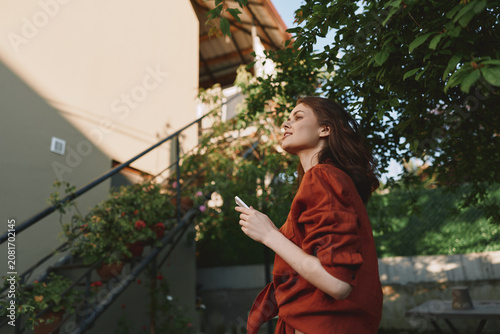 Foto A woman in a red coat stands outdoors, looking up with a phone in hand