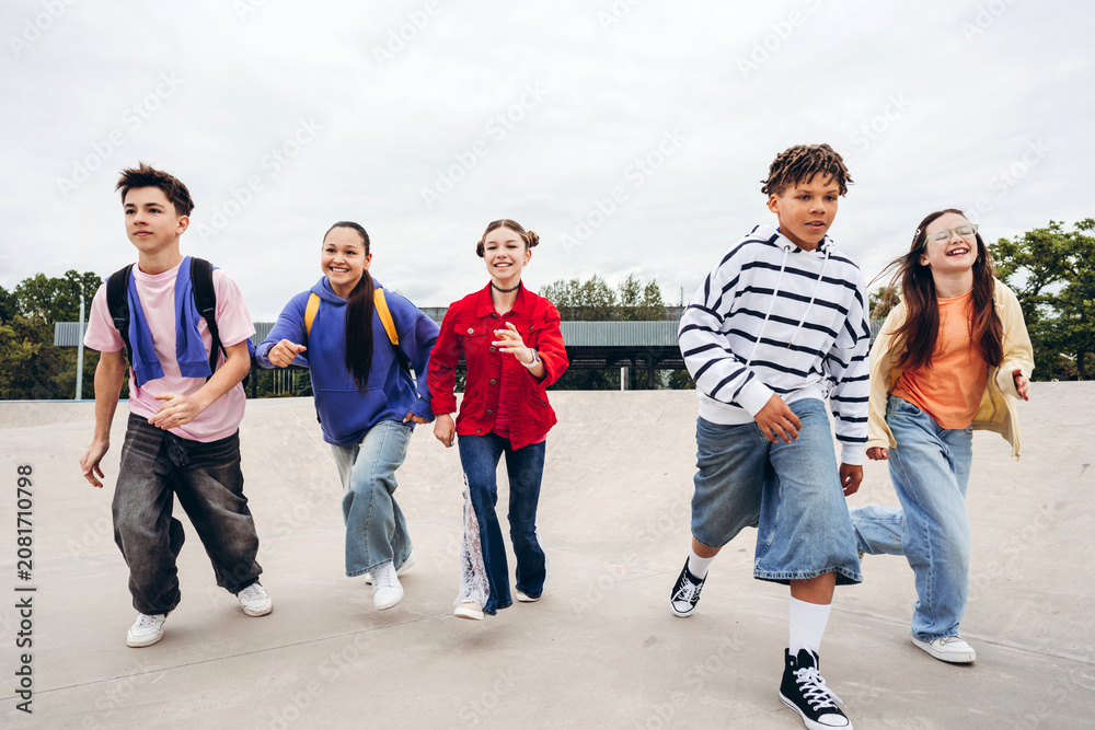 Obraz premium Group of happy multicultural teenagers running together at skate park outdoors
