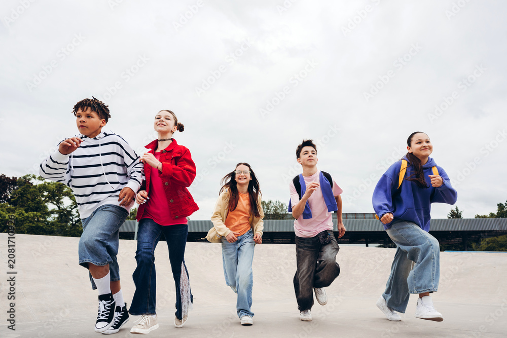 Obraz premium Portrait of happy group of teenagers running together in urban skate park