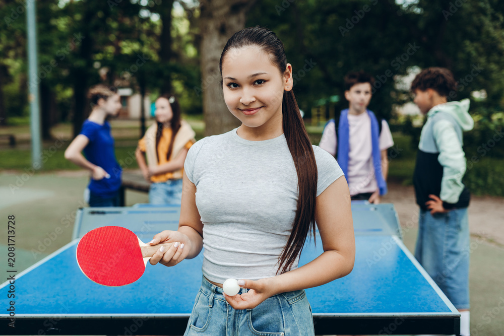 Obraz premium Portrait of smiling teenage girl holding table tennis paddle and ball outdoors
