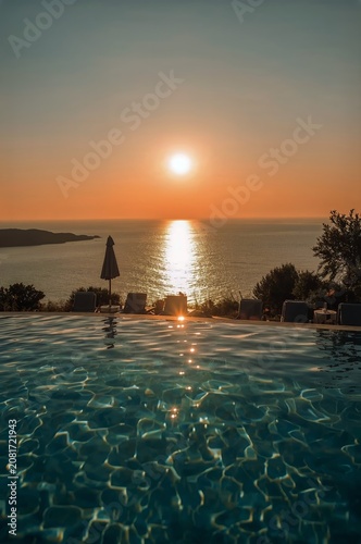 Sunset Over the Ocean Seen From a Poolside With Chairs and Umbrella in the Ba...