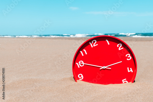 a red clock sinks into the sand on an empty beach