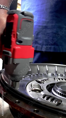 Close up of a technician's hand operating a cordless impact driver to tighten bolts on a large metallic clutch assembly or torque converter.