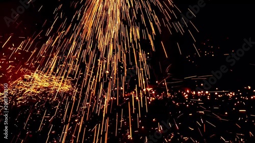 Bright yellow and orange fiery sparks showering down and scattering across a dark surface during an industrial metalworking process.