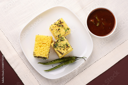 Khaman Dhokla made up of rice chana dal is a popular breakfast or Snacks recipe from Gujarat, India, served with Green chutney and fried chilli.. Selective focus
