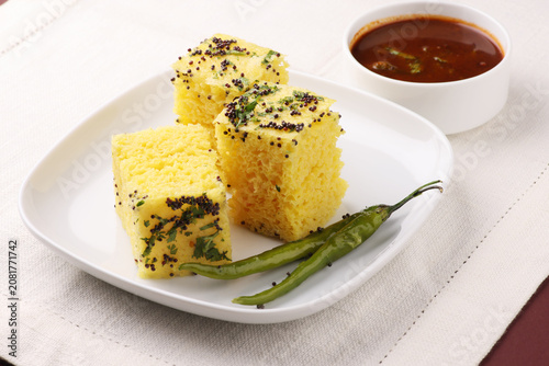 Khaman Dhokla made up of rice chana dal is a popular breakfast or Snacks recipe from Gujarat, India, served with Green chutney and fried chilli.. Selective focus
