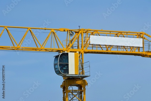 Canvastavla The operator cabin and jib of a bright yellow tower crane stand out against a clear blue sky