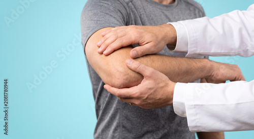 Doctor examining elbow of patient in medical office closeup professional physical therapy care.