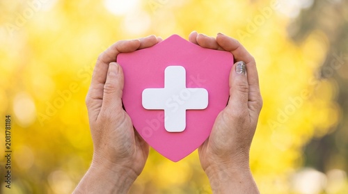 Hands holding pink shield with white cross, protection symbol outdoors