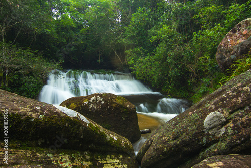 small waterfall in the forest with rock in front background