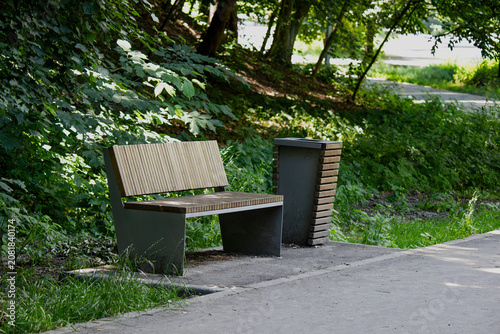 Modern wooden bench and trash can in a sunny summer park