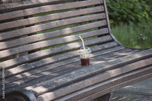Plastic cup with leftover iced coffee on an old wooden park bench