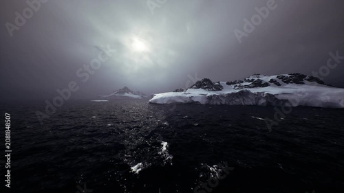 moody arctic voyage under low sun and heavy cloud, rough seas with spray and whitecaps, distant ice shelf partially shrouded in mist, sense of urgency