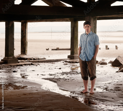 Tableau sur toile Portrait of young man standing under boardwalk on a beach