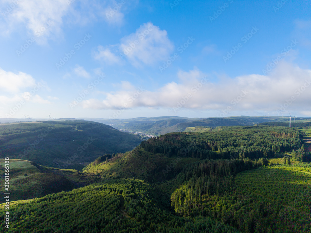 Fototapeta premium Aerial View of South Wales Valleys with Dense Forest Covered Mountains with Blaenrhondda Village in the Distance. 