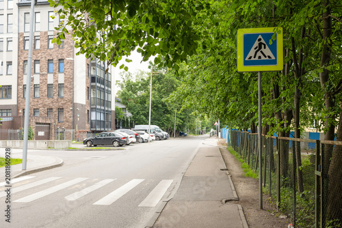 City street with a marked pedestrian crossing, traffic signs and tree-lined sidewalk. Safe urban transportation infrastructure suitable for concepts of road safety, mobility, city planning and