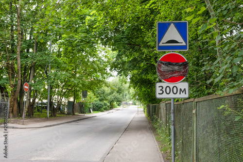 Canvastavla Collection of traffic signs including a speed bump warning and road restriction sign installed along a tree-lined urban road