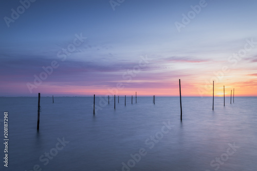 Foto Minimalist landscape photograph featuring a series of wooden poles emerging from the calm waters of Markermeer near Volendam in North Holland, Netherlands