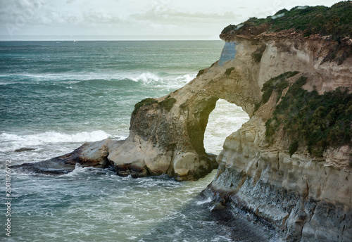 Sea-carved rock arch on a rugged coastline with crashing waves on the evening