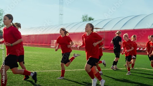 Womens soccer team conditioning on artificial turf field during high-intensity pregame training run, athletes in red uniforms building endurance and teamwork