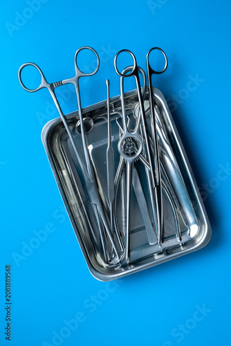 Sterile surgical instruments and tools - scalpels, scissors and others - in a stainless tray on blue background, top view