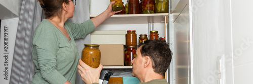Photos A married couple is busy placing canned goods on shelves in their pantry