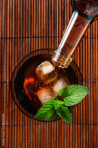 Chinotto soft drink with ice and fresh mint in glass on dark wooden background