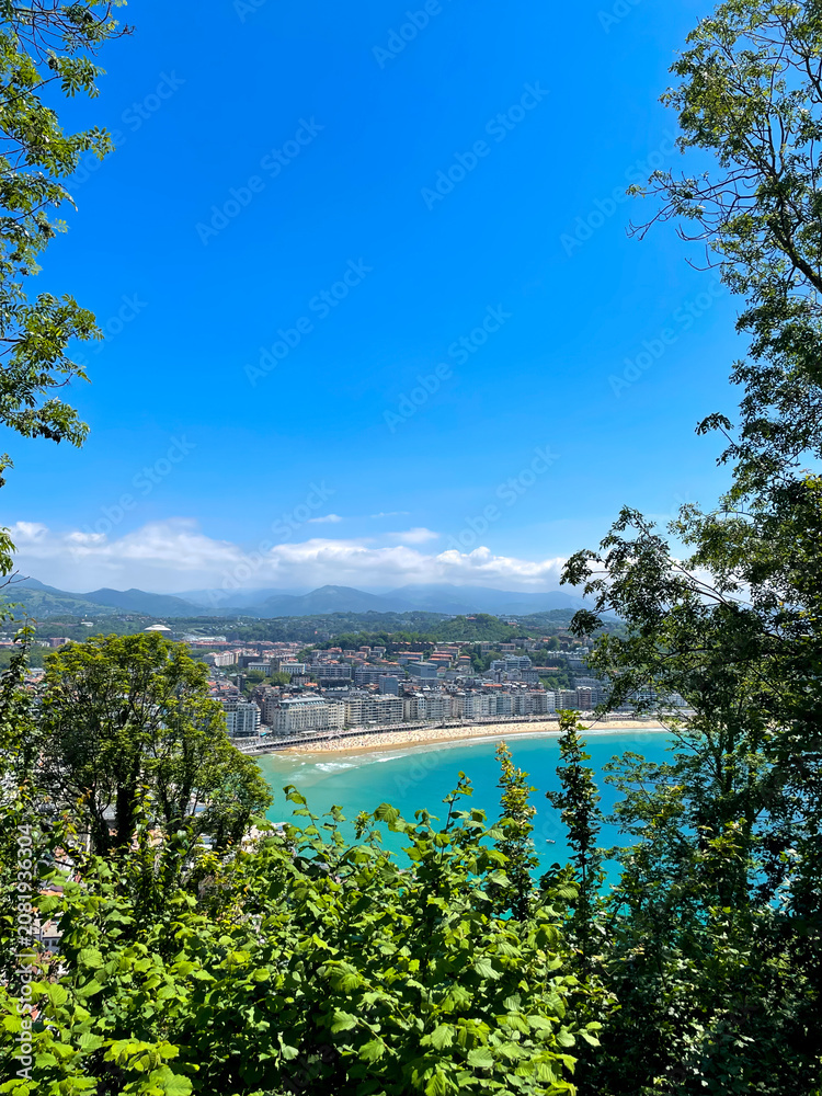 Fototapeta premium La Concha Bay panorama from Mount Urgull above sunny San Sebastian coastline and mountains, Spain