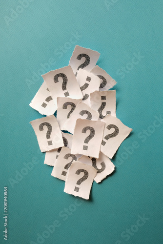 Vertical pile of white paper notes with question marks forming a column on blue backdrop