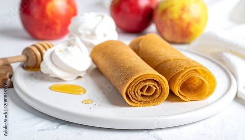 A plate of golden brown rolled crepes with whipped cream and honey