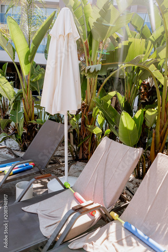 Obraz na płótnie Empty sun loungers with towels and water blasters under folded beach umbrella, s